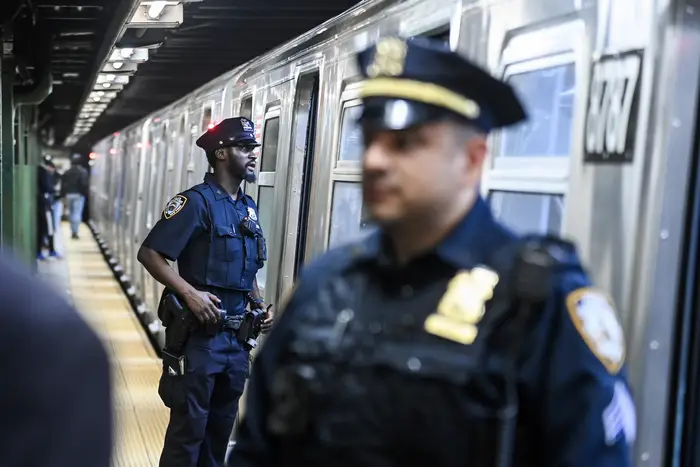 NYPD officers stand outside a subway train.